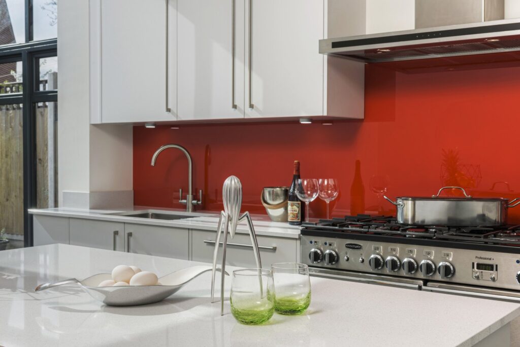 Professional kitchen installation in Hadley Wood featuring a red glass splashback and a quartz worktop as the main focal points.
