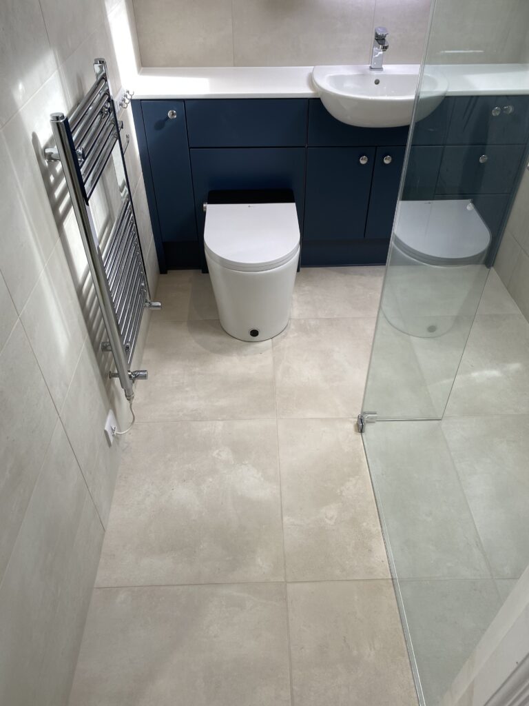 Professional wet room installation in Totteridge featuring a blue vanity unit and a chrome towel rail as the main focal points