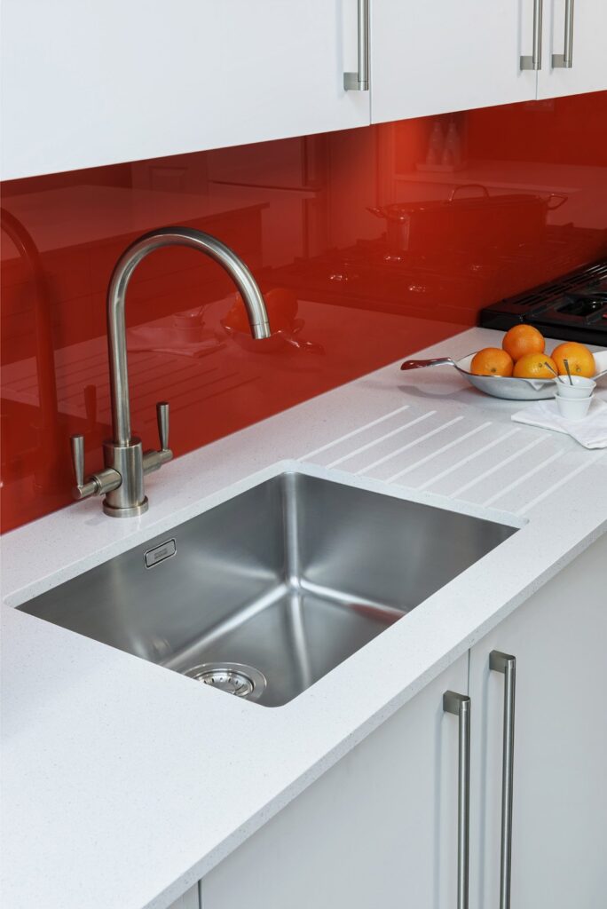 Professional kitchen installation in Hadley Wood featuring a red glass splashback and an under mount sink as the main focal points.