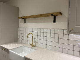 Professional kitchen installation in Totteridge featuring a wood shelve and a square tiles as the main focal points. The design is completed with a gold kitchen tap and a belfast sink for a cohesive modern finish. Project completed by A Martens Kitchens & Bathrooms Ltd. For a free quote, visit https://amartens.co.uk to discuss your kitchen renovation. Professional kitchen installation in Totteridge featuring a wood shelve and a square tiles as the main focal points